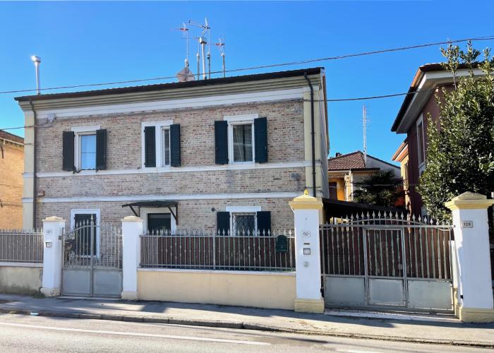 Casa in mattoni a due piani con cancelli metallici e persiane verdi.